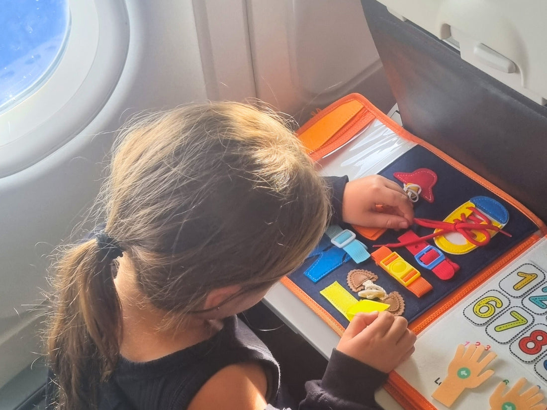 girl sitting on a couch playing with her pink Milleli busy board in her room. she is concentrated on the buckle toy