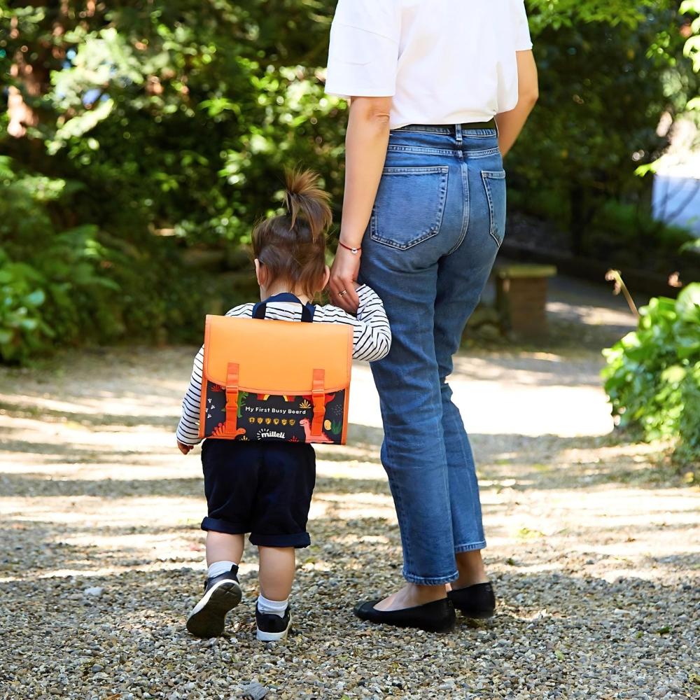 Mom holdng toddler hand while son wearing the Milleli My First Busy Board backpack with 20 montessori activities for toddlers